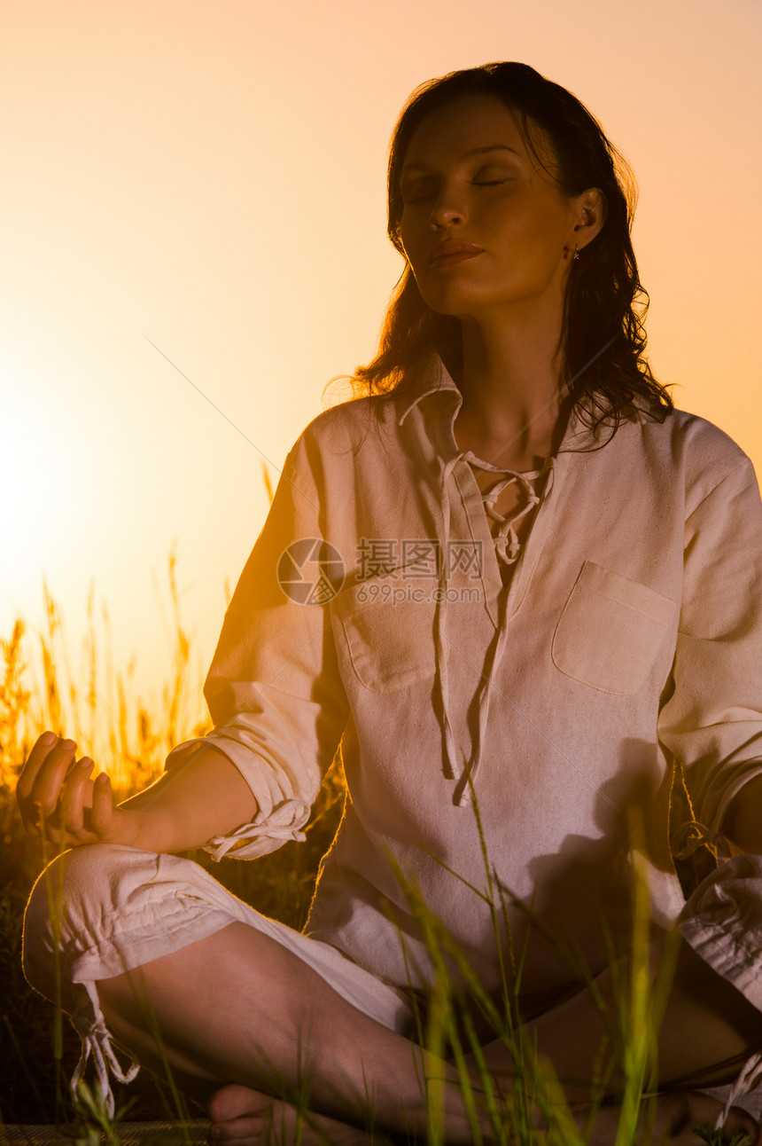 美丽的瑜伽女人坐日出阳光围绕着她图片