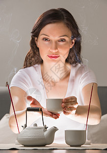 轻的女人坐冥想姿势前的茶具香气棒放松的图片