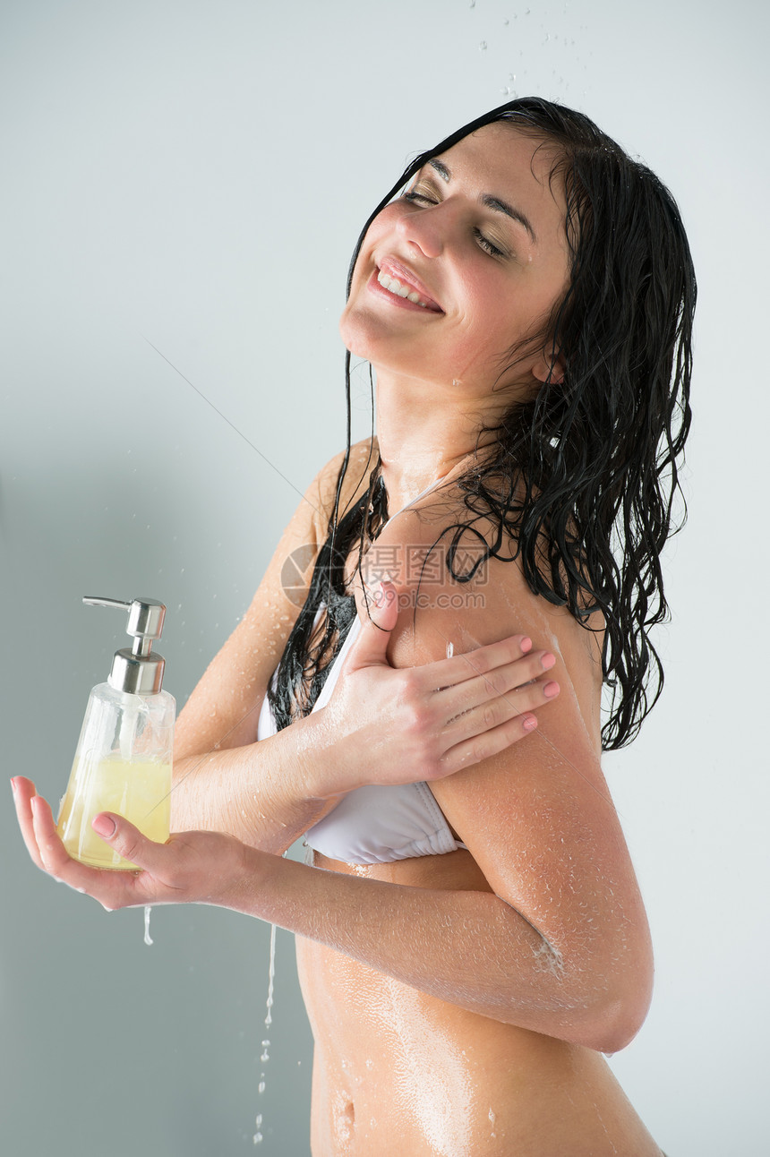 美丽的女孩洗澡着装淋浴凝胶的璃瓶,水溅时清洗自己图片