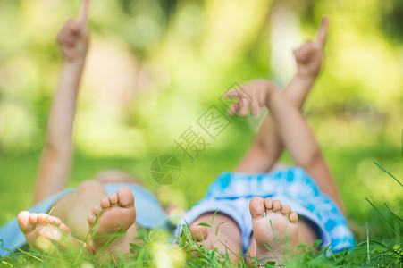 孩子躺绿色的草地上指着夏天公园里的天空图片