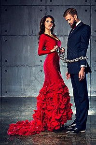 轻的快乐的女人穿着红色的衣服,抱着男人沉重的链子上优雅的晚装背景图片