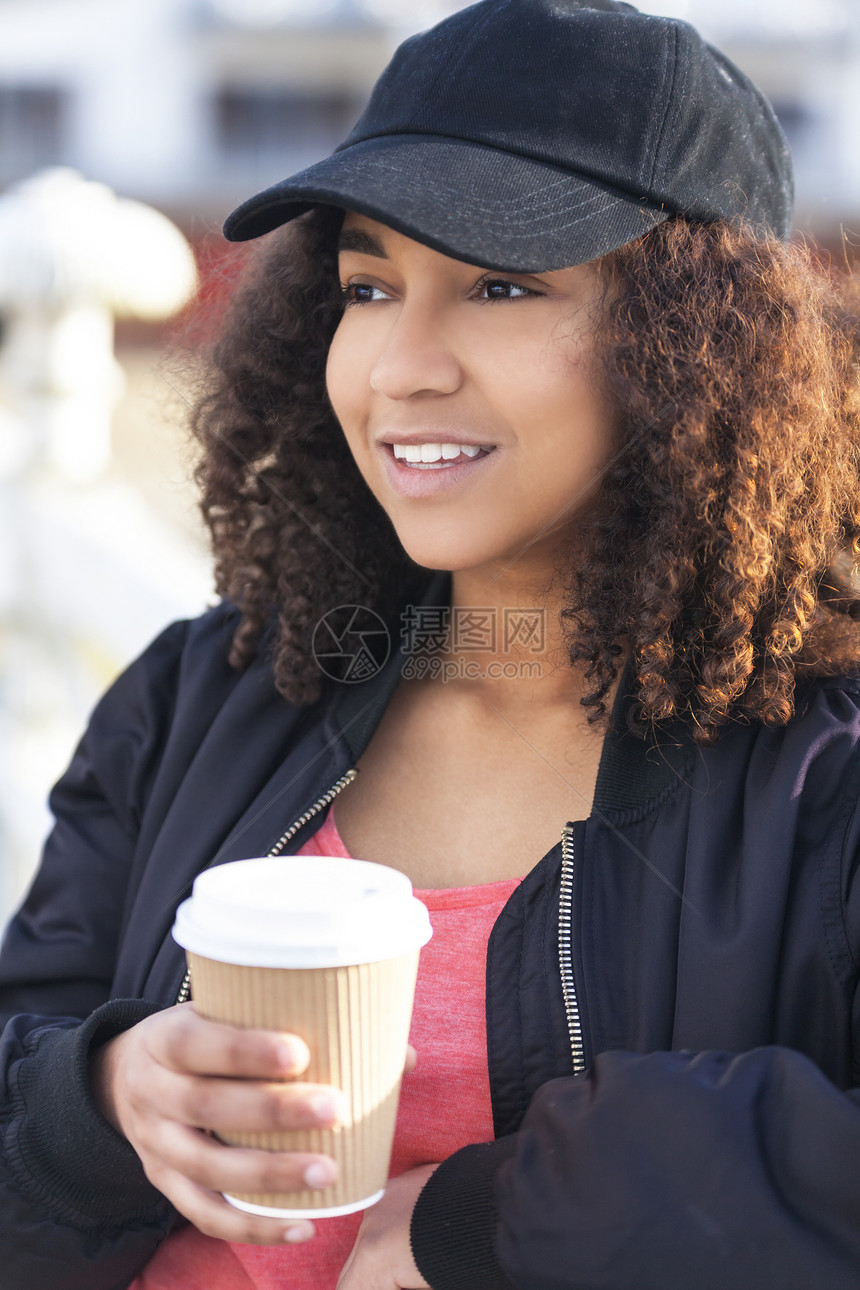 美丽快乐的混合种族非裔美国女孩十几岁的女青,微笑着喝着外卖咖啡,外戴着黑色棒球帽轰炸机夹克图片