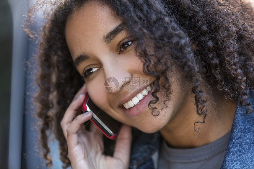 户外肖像美丽的快乐混合种族非裔美国女孩十几岁的女轻女子微笑与完美的牙齿手机上交谈图片