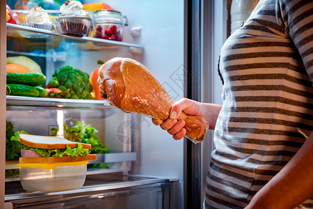 饥饿的胖女人手里着条大火鸡腿,站打开的冰箱旁边健康的食物图片