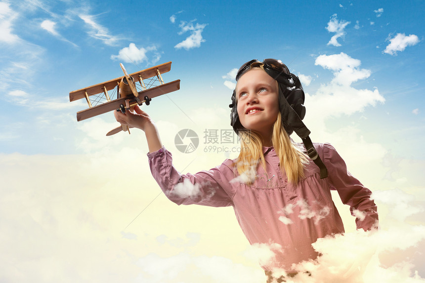 飞行员头盔中的小女孩云背景下玩玩具飞机的形象图片
