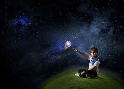 男孩指着主意可爱的学校男孩坐草地上,用手指触摸璃灯泡图片