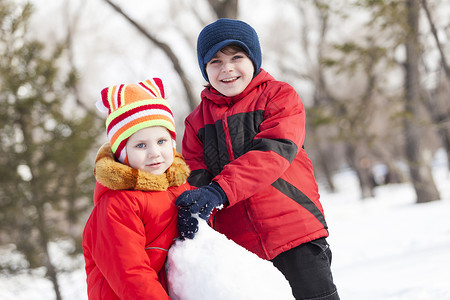 可爱的男孩女孩冬季公园堆雪人冬季活动游戏图片