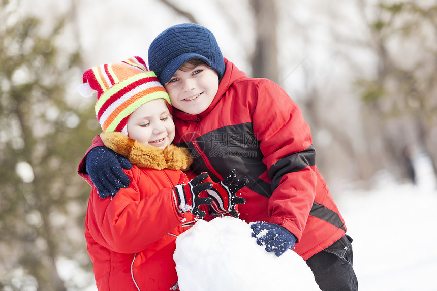 可爱的男孩女孩冬季公园堆雪人冬季活动游戏图片