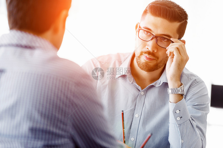 坐办公桌前的吸引力的上族轻的商人坐办公室的桌子上他的同事交谈图片