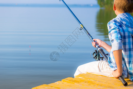 穿着蓝色衬衫的男孩坐海边的码头上,着鱼竿高清图片