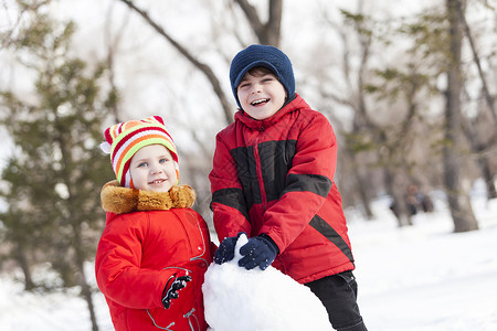 可爱的男孩女孩冬季公园堆雪人冬季活动游戏图片