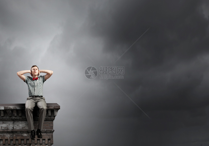 轻人坐建筑物的顶部,用手捂住耳朵图片