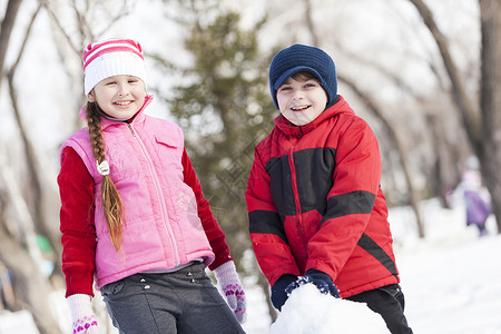 可爱的男孩女孩冬季公园堆雪人冬季活动游戏图片