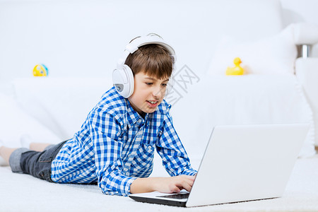 孩子享受闲暇时间学龄男孩躺地板上,耳机听笔记本电脑上的音乐图片