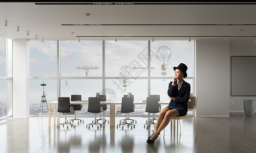 坐办公室椅子上的女商人优雅的女商人穿着西装,戴着帽子,坐办公室椅子上图片