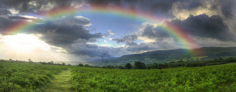 惊人的夏季日落与彩虹跨越乡村悬崖景观背景图片
