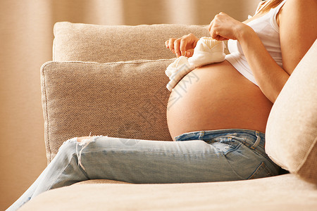 孕妇抱着小婴儿鞋家沙发上放松图片