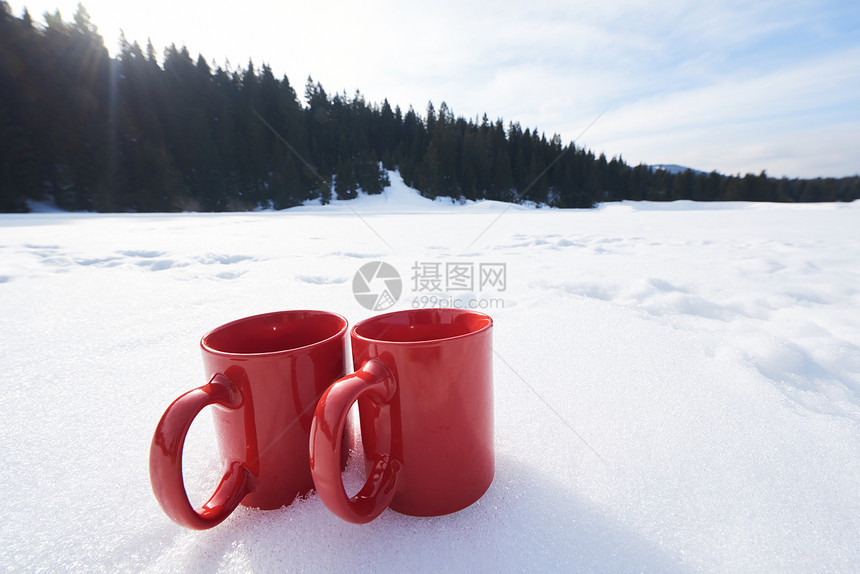 两辆红色的热茶饮料雪中,美丽的冬季阳光明媚的天,与木屋森林的背景图片