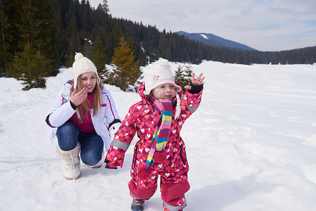 快乐的家庭寒假,妈妈可爱的小女孩玩得很开心,边滑边下雪图片