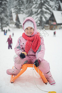 雪与小女孩可爱的小女孩的肖像,坐雪橇冬季与新鲜的雪,吃饼干休息背景