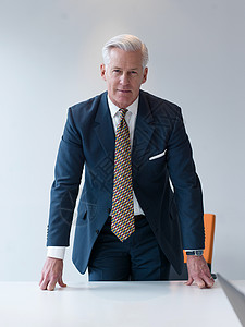 自信而英俊的高级商人站现代办公室会议室的桌子后图片
