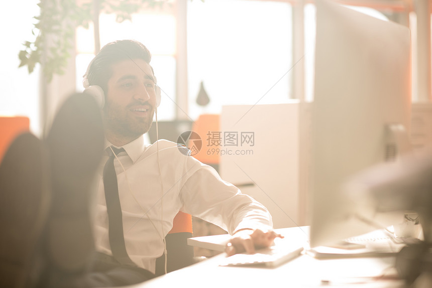快乐的轻阿拉伯商人,留着胡子,现代初创公司办公室听耳机上的音乐图片