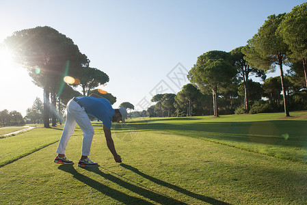 高尔夫球运动员把球放发球台上背景中高尔夫球场景观上美丽的日出图片