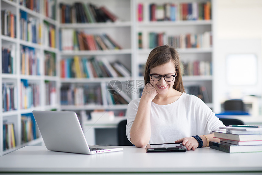女学生用笔记本电脑图书馆学,并互联网上搜索信息图片