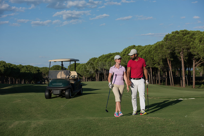 轻夫妇步行高尔夫球场的下个洞带高尔夫球袋的人图片