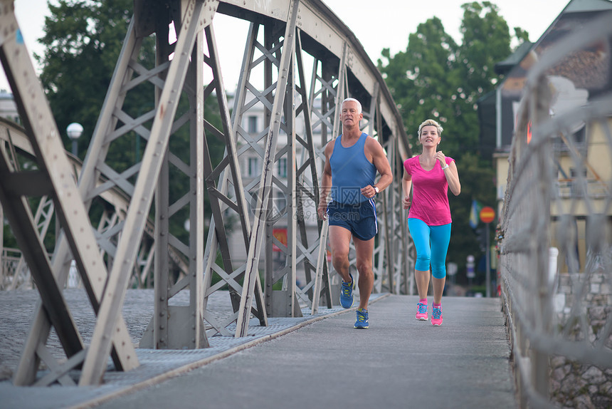 健康成熟的夫妇清晨城市慢跑,背景为日出图片