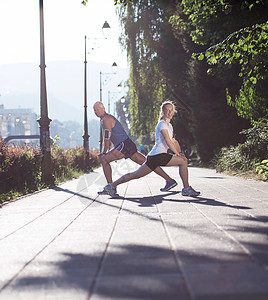 慢跑夫妇热身伸展之前,晨跑训练锻炼城市与日出背景图片