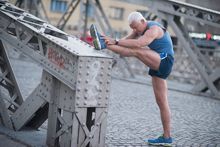 英俊的老人清晨慢跑锻炼前伸展热身图片