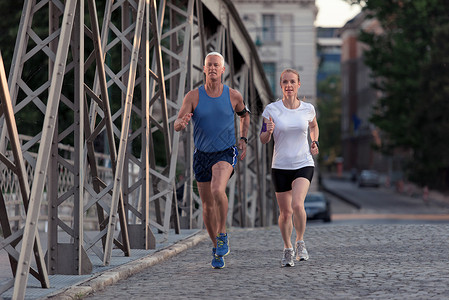 健康成熟的夫妇清晨城市慢跑,背景为日出高清图片