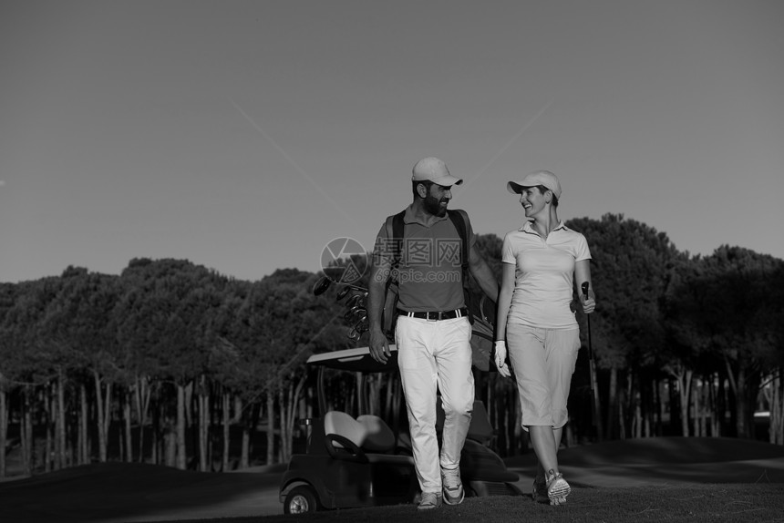 轻夫妇步行高尔夫球场的下个洞带高尔夫球袋的人图片