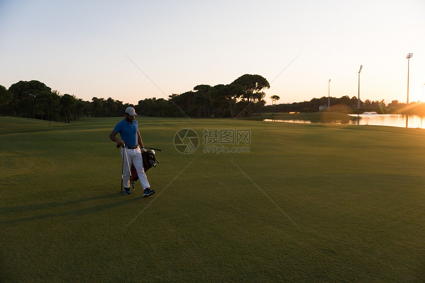 英俊的中东高尔夫球手背着包,美丽的日落背景下步行高尔夫球场的下个洞图片