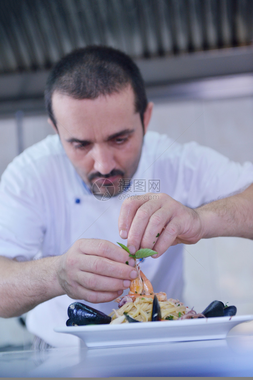 英俊的厨师穿着白色制服装饰意大利沙拉海鲜鱼现代厨房图片