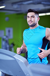 英俊的男人现代健身房的跑步机上跑步图片