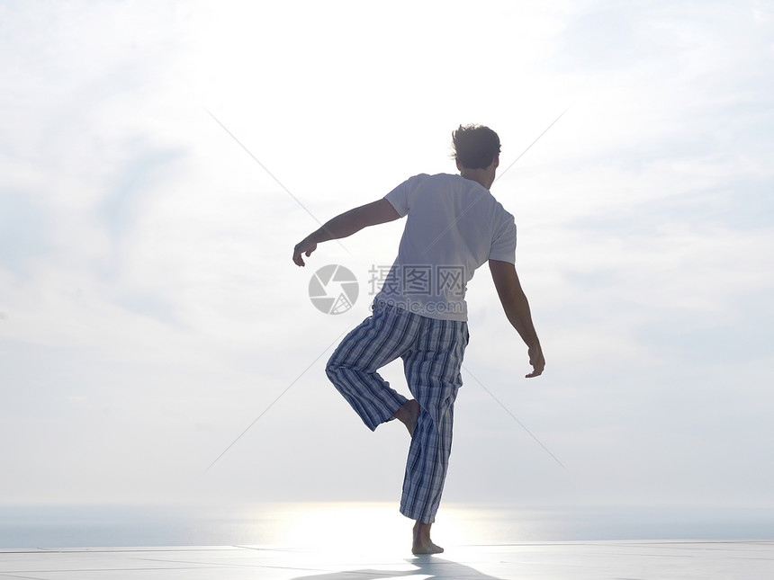英俊的轻人现代家庭泰勒斯练瑜伽,背景海洋日落图片