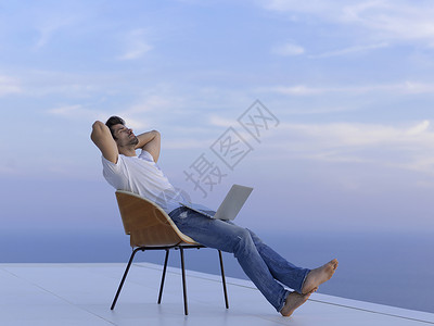 英俊的轻人放松工作笔记本电脑家里的阳台,同时看日落图片