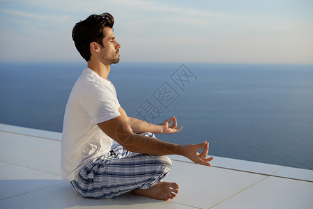 阳台瑜伽英俊的轻人现代家庭泰勒斯练瑜伽,背景海洋日落背景