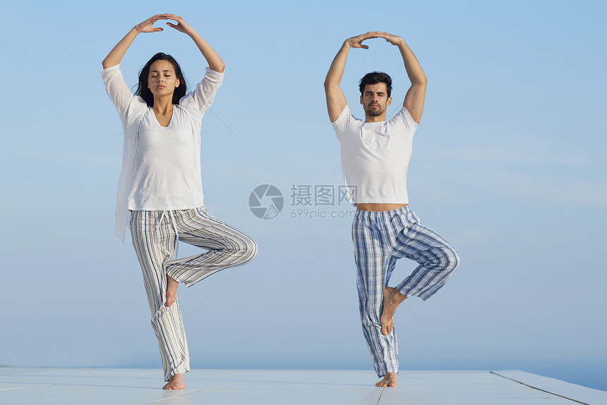 轻的夫妇日落时练瑜伽,现代的家庭梯田与海洋日落的背景图片