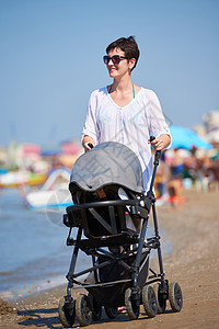 快乐的轻母亲海滩上散步,推着婴儿车背景