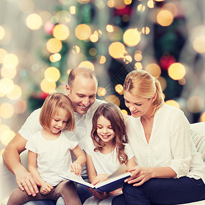 家庭,童,假期人微笑的母亲,父亲小女孩客厅诞树背景上看书图片