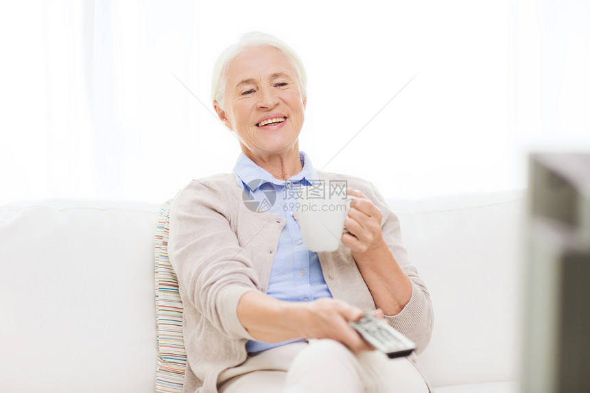 技术电视龄人的快乐的老妇女家遥控器看电视喝茶换频道图片