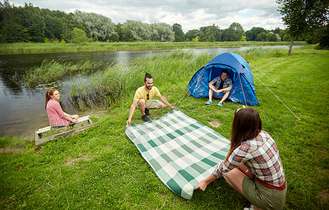 野营,旅游,徒步旅行人们的快乐的朋友与帐篷铺设野餐毯营地河岸图片