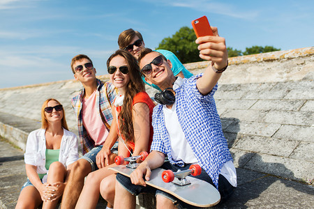 友谊,休闲,夏天,技术人的群微笑的朋友与滑板智能手机户外自拍图片