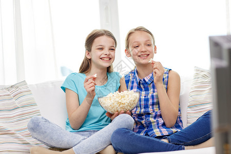 人,孩子,电视,朋友友谊的两个快乐的小女孩电视上看喜剧电影,家吃爆米花图片