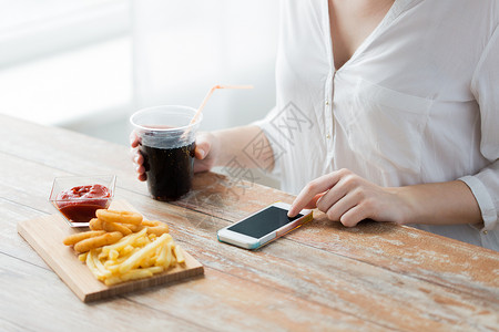 快餐,人,技术饮食密切妇女与智能手机喝可乐吃薯条,番茄酱油炸鱿鱼戒指木桌上图片