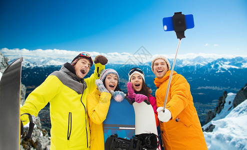 冬季运动,休闲,友谊,技术人的快乐的朋友与滑雪板拍照智能手机自拍杆雪山背景图片