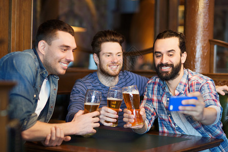 人,男人,休闲,友谊技术快乐的男朋友酒吧酒吧喝啤酒用智能手机自拍背景